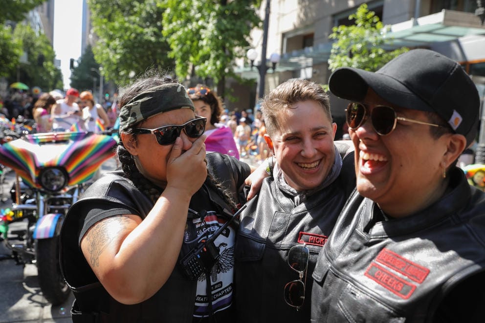 Three women laugh together, all wearing black leather motorcycle vests