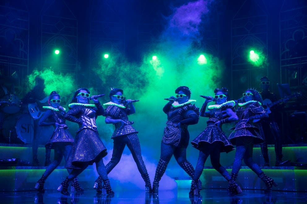 a theatrical stage moment with six women doing a dance move under dramatic lights