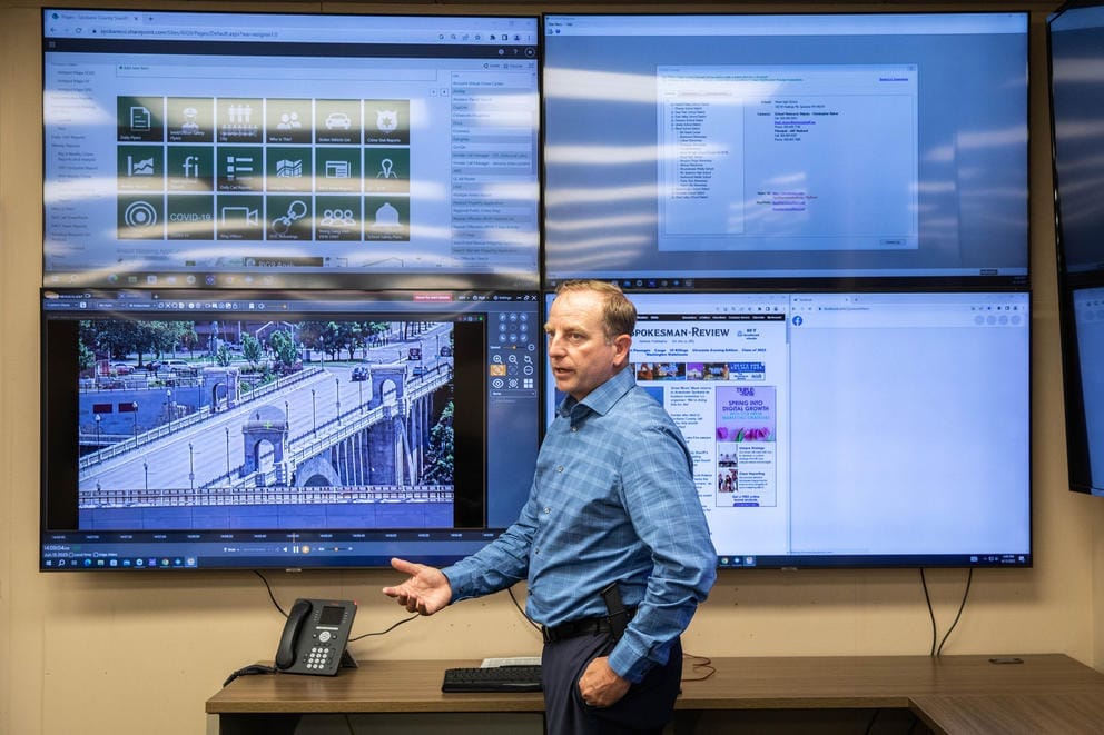 Lt. Justin Elliott stands in front of four large video monitors on the wall.