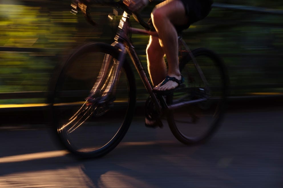 A close up of feet in sandals pedaling a moving bicycle in the evening sun