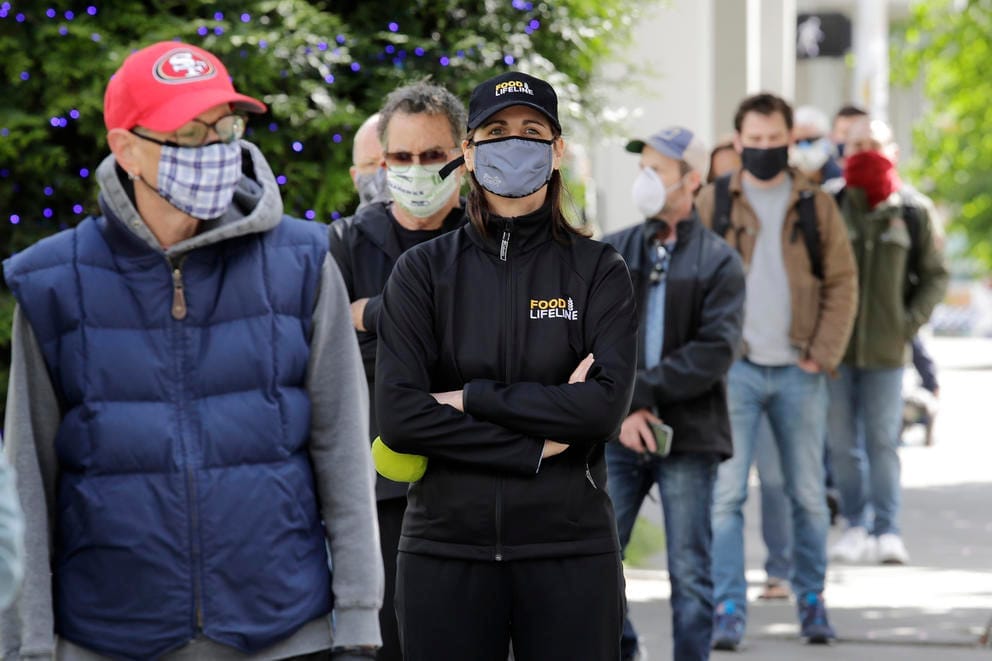 A line of customers wearing protective masks waits to enter the West Seattle Farmers Market