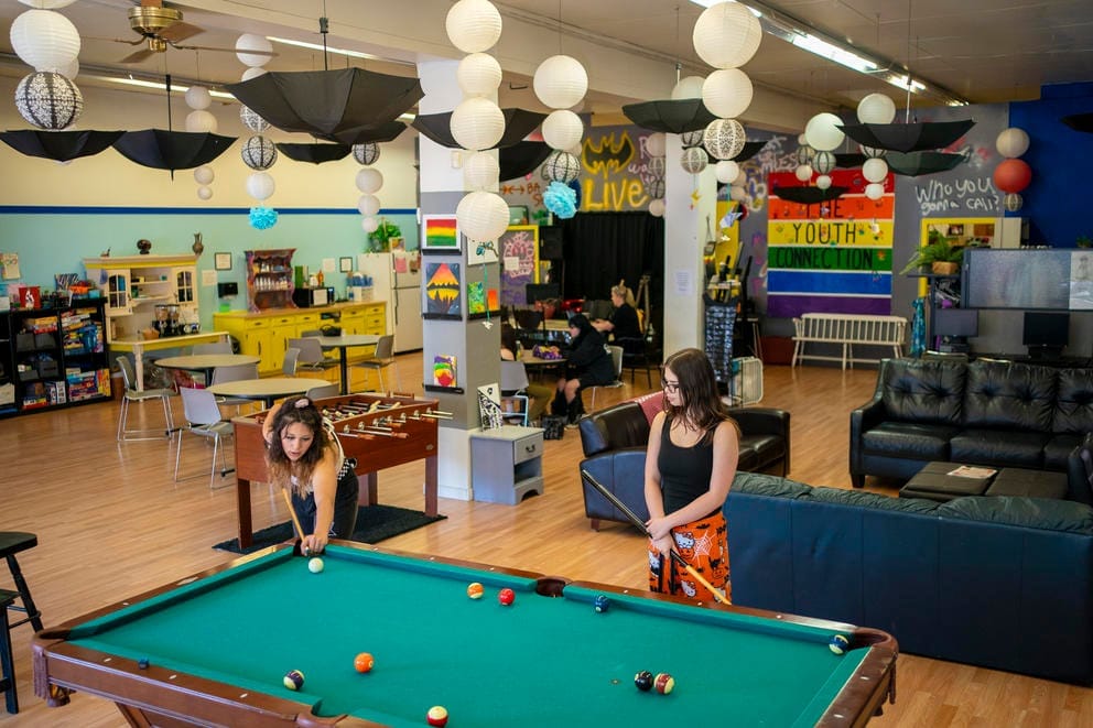 Two teens play pool in a brightly decorated lounge area at The Youth Connection.