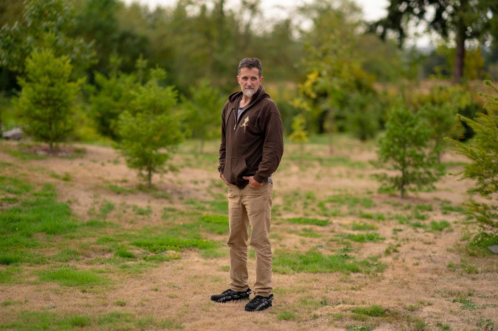 A man stands outside surrounded by patches of grass and trees