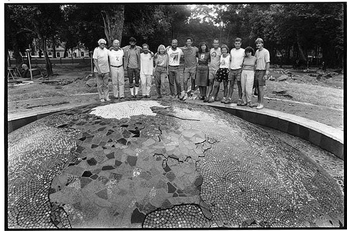 A group of people in a park line up behind a sculpture that is low to the ground.
