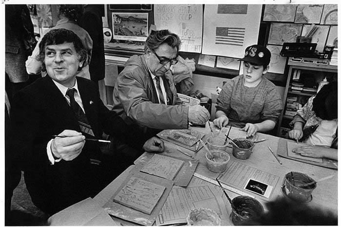 Two adults and a child sit at a table and paint tiles.