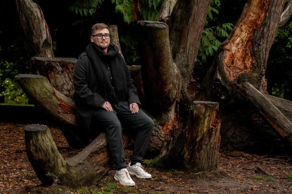 Daniel Lugo sits for a portrait among a stand of trees.