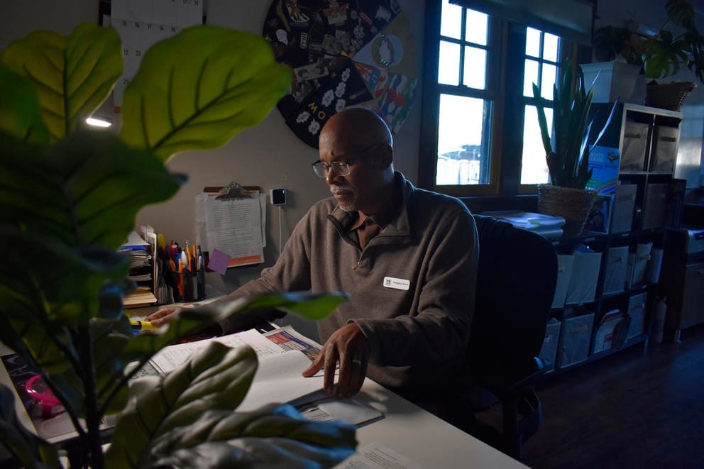 A person in a gray sweater looks over papers sitting at a desk.