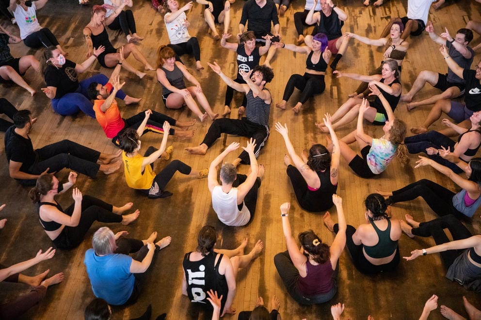 A group of people sit on the floor in a dance circle