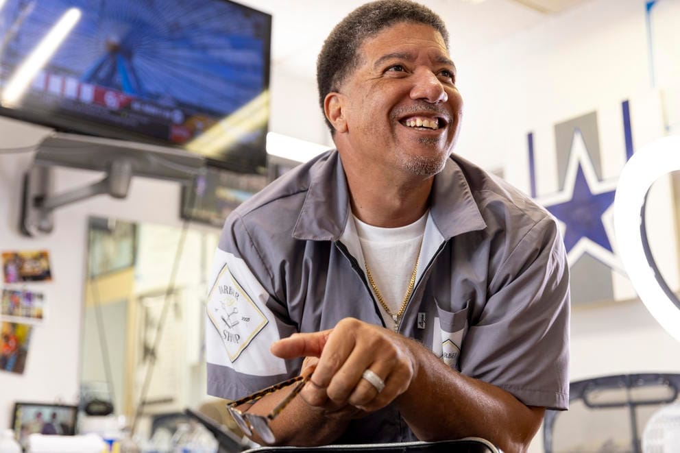 Cliff “C.J.” Jones leans over a chair and smiles in his barbershop