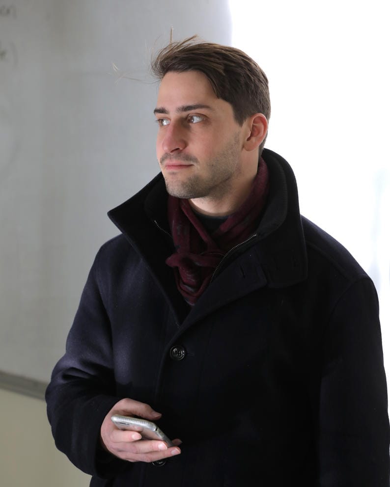 A medium shot of a man standing in a black jacket holding a recorder