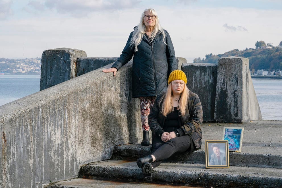 Pam Felton, left, and Lucy Felton, the mother and sister of Harold Felton (seen in the framed photos) pose for a portrait on stairs near the water