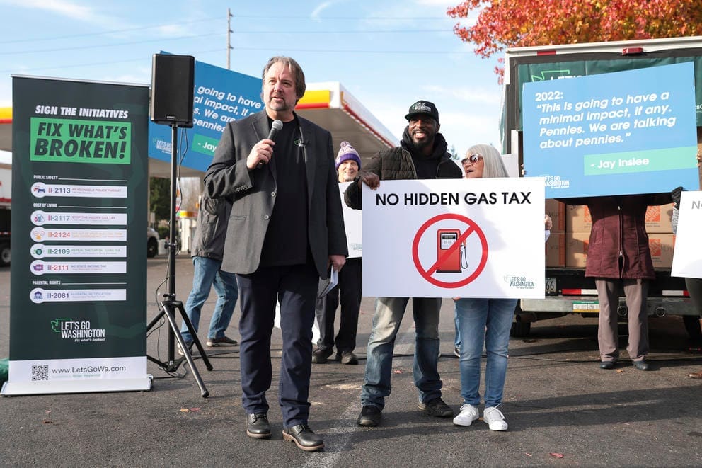 A man with a microphone stands with a group of demonstrators holding signs