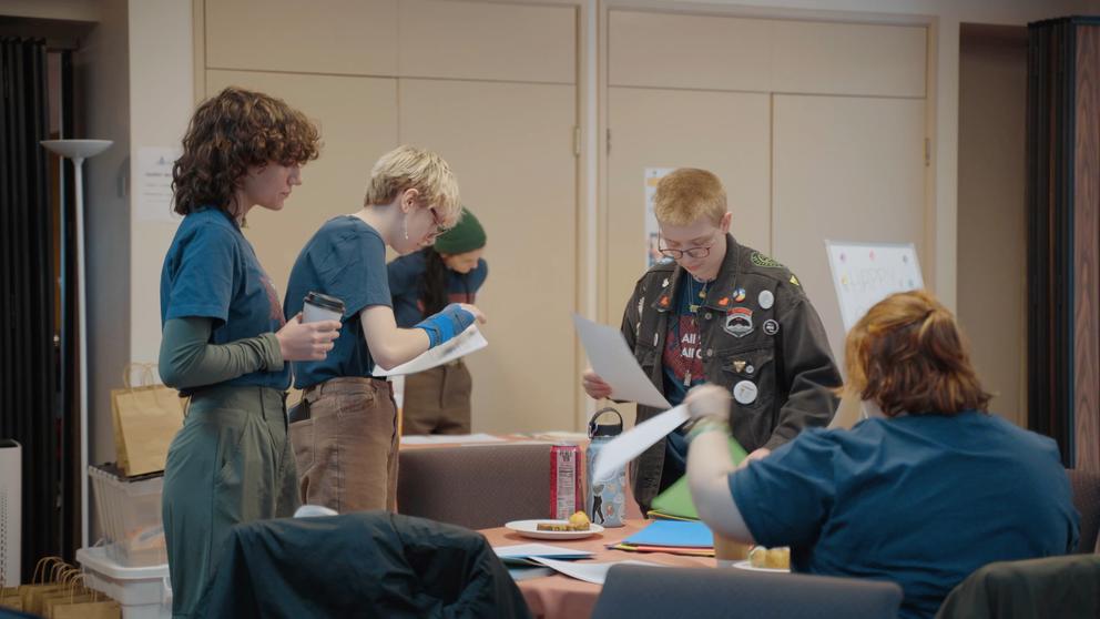 Four people review papers in a conference room.