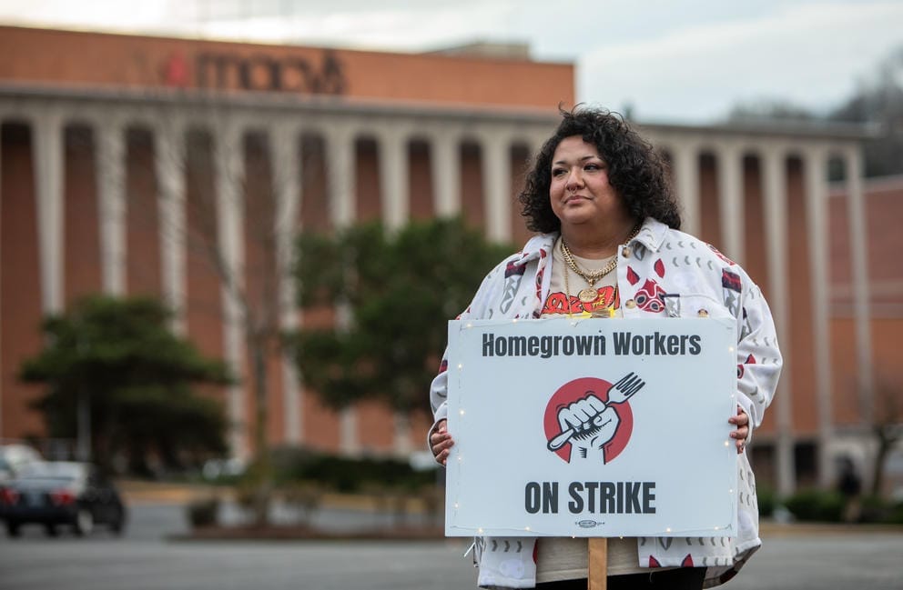 A person holding a sign stands for a portrait outside the Westfield Southcenter mall.