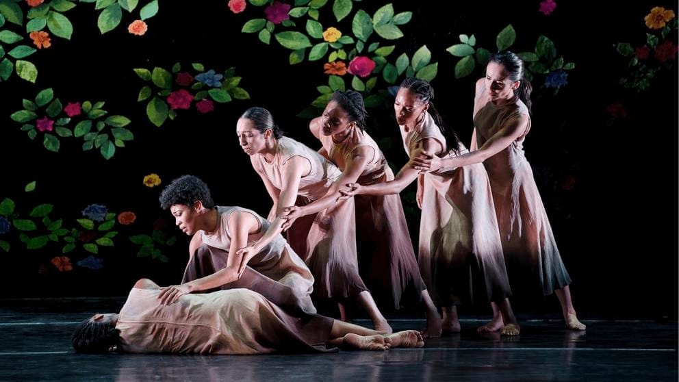 photo of six female dancers on stage in long dresses, each bending over in a line