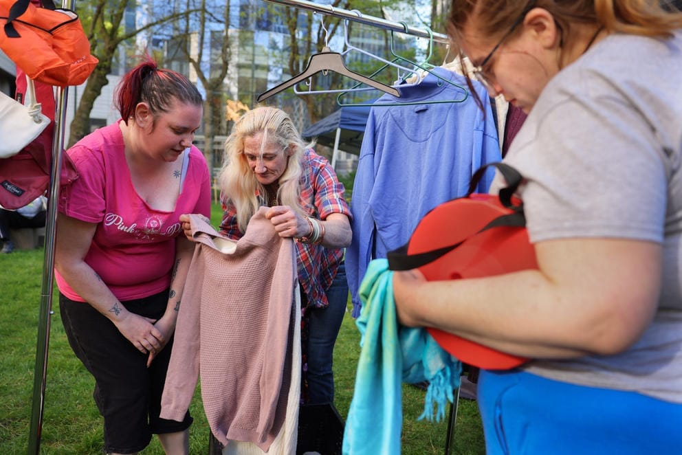 three people sort through a colorful rack of clothing 