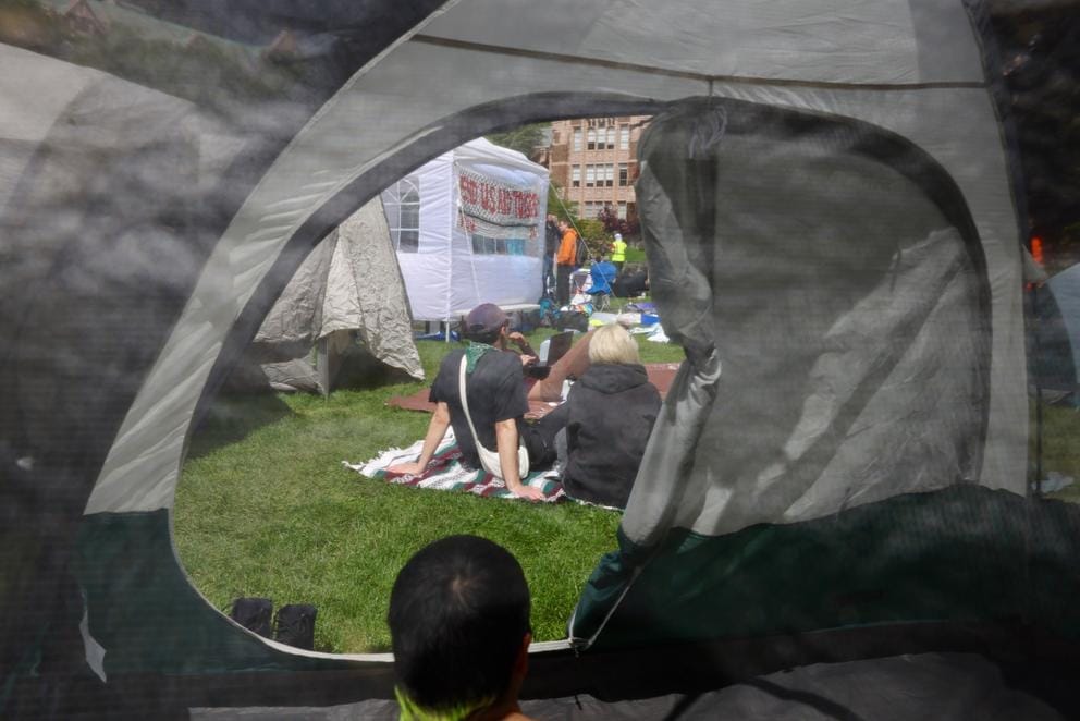 Students sit inside and outside of a tent at the encampment