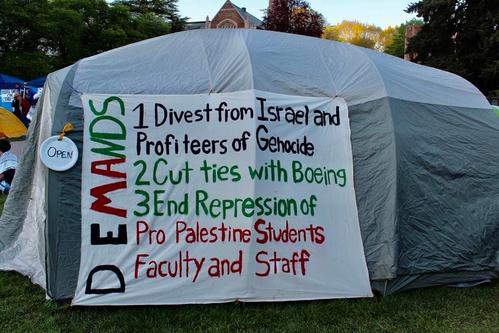 A hand-written sign at the University of Washington encampment in solidarity with Gaza rests against a tent