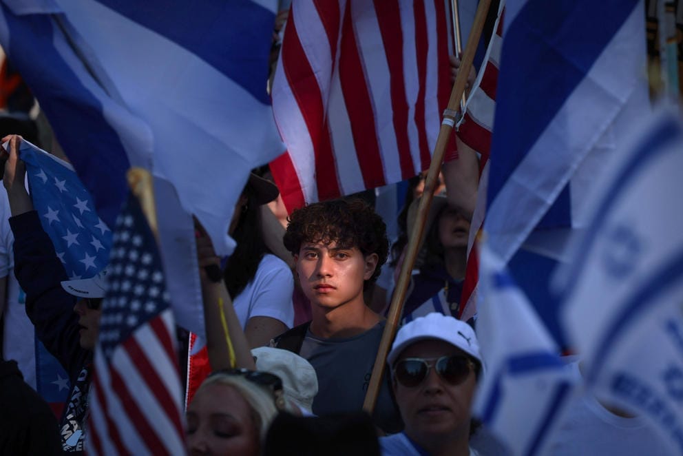 A face is illuminated in a sea of Israeli and American flags