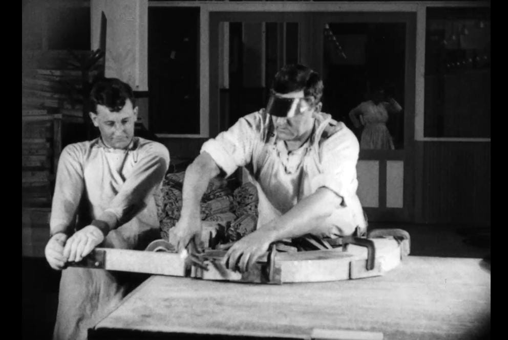 Two men bend wood during construction of an airplane.