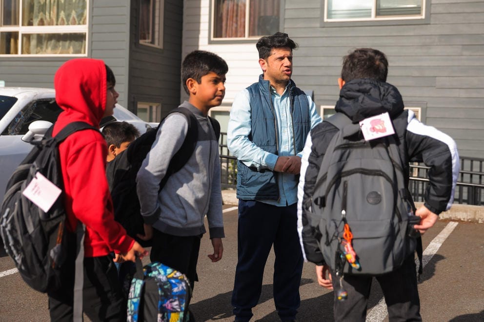 Ahmad Heyadee talks with his son Baheer, 10, and his friends as they wait for a late bus to pick them up for school outside their apartment complex in Des Moines.