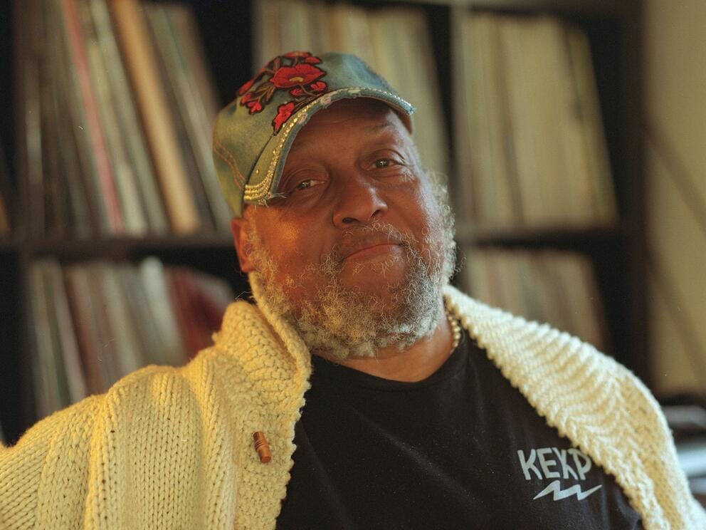 photo of a bearded man in a baseball hat standing in front of record shelves