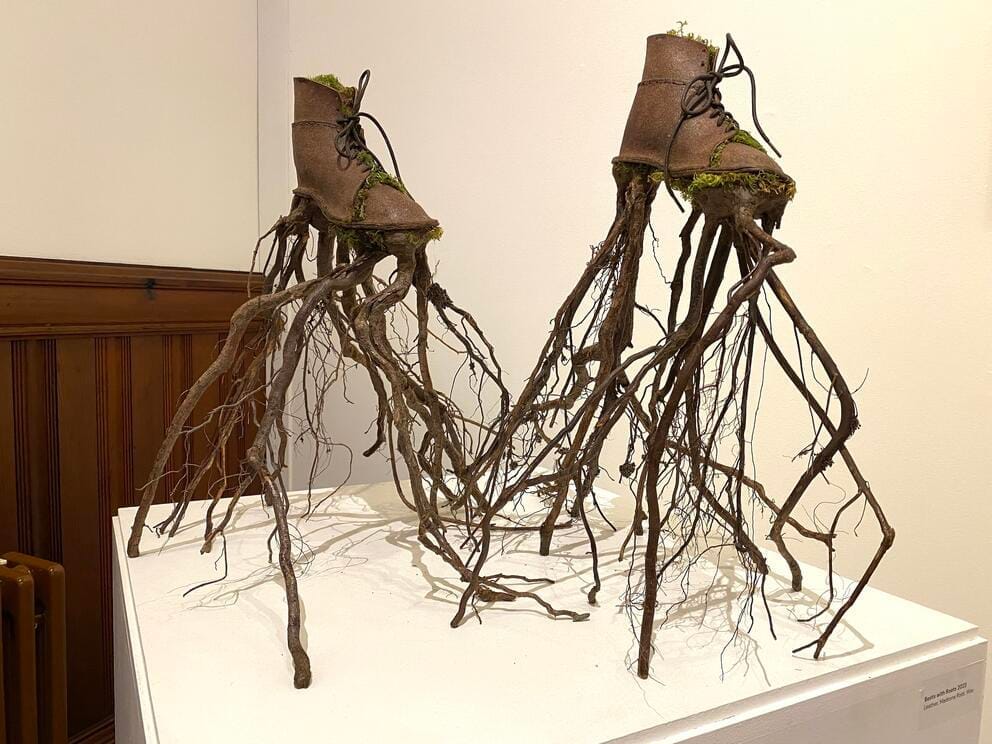 photo of an artwork made of old work boots that seem to have sprouted roots