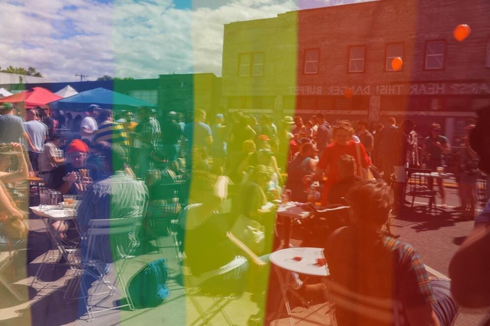 a group of people gathered on the street, seen thru the colors of a rainbow flag