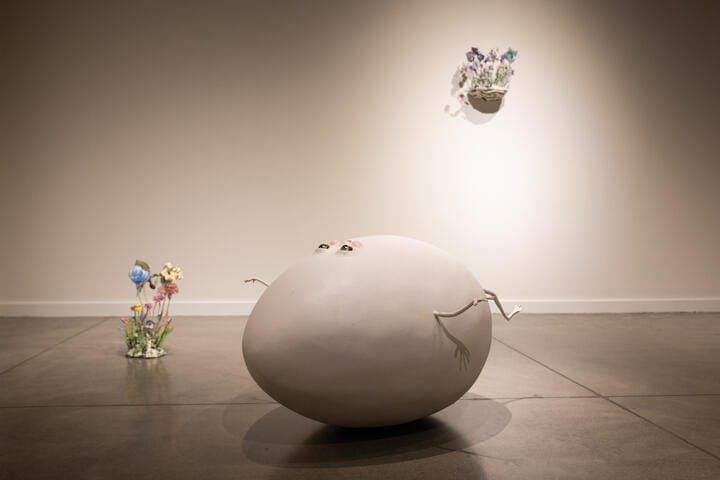 A large sculpture resembling an egg with arms and eyes in a gallery.