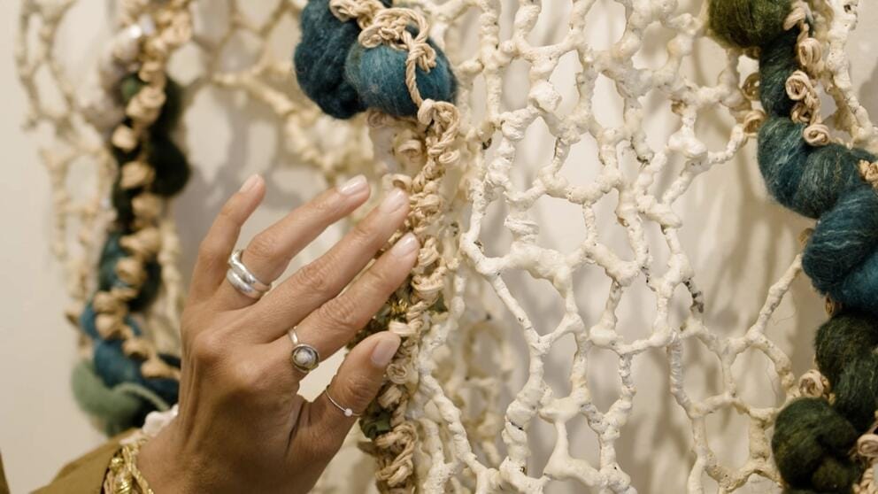close up of a woman's hand next to a netlike wall hanging
