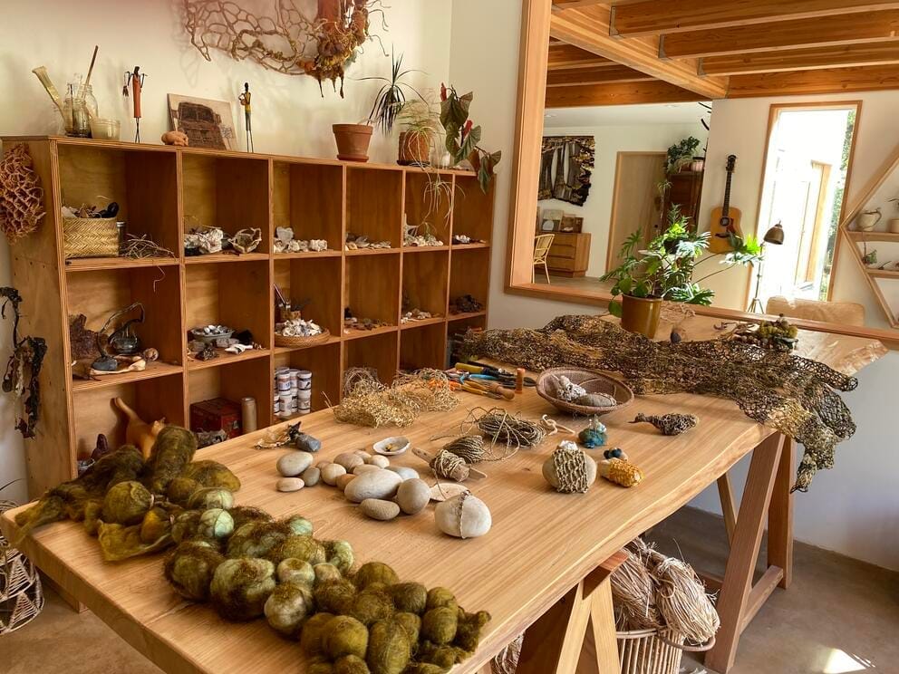 photo of an art studio with shelves and a table full of natural fibers and beach finds