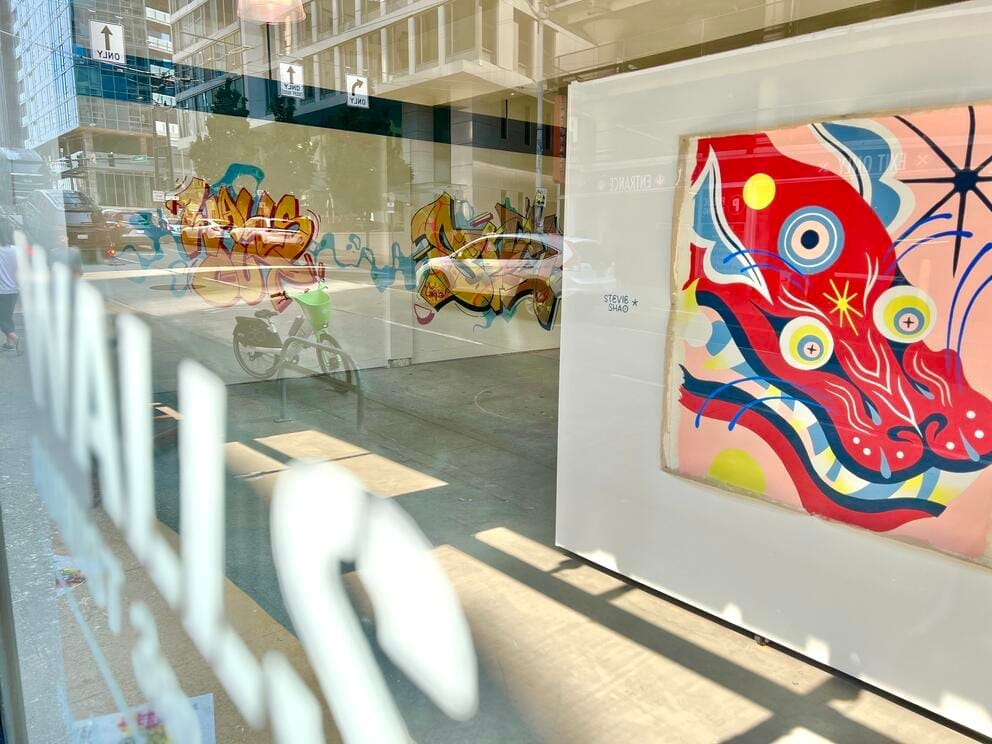photo from outside peering in thru a gallery window where a large pink-red dragon appears on a wall