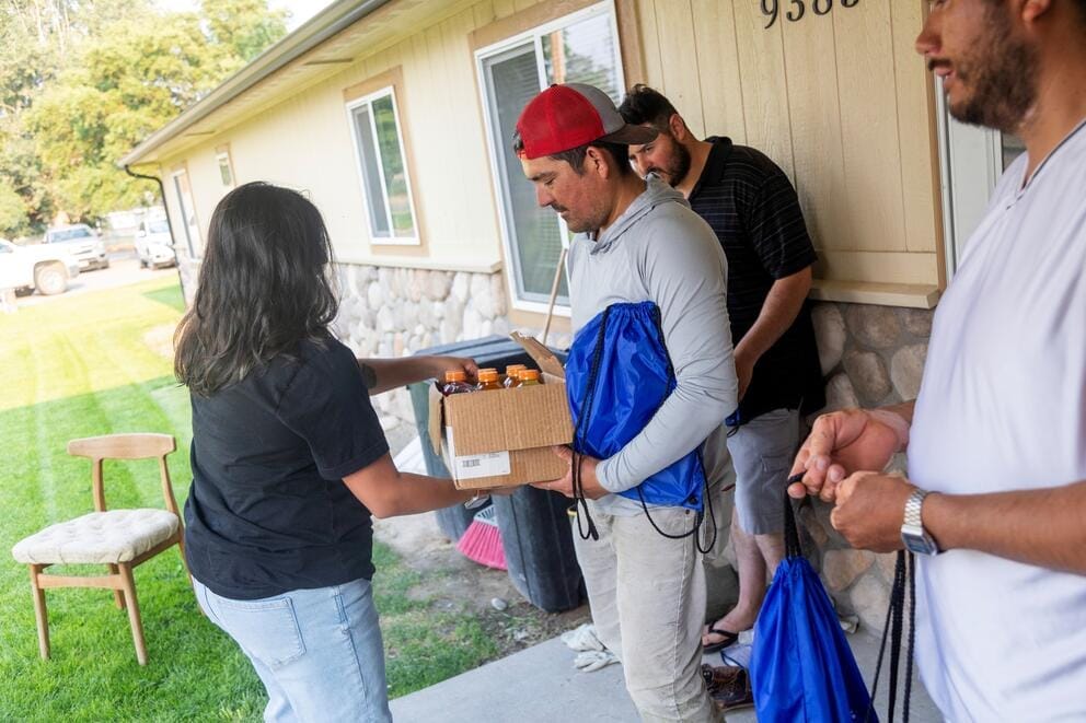 A person hands over a box of drinks to another person.