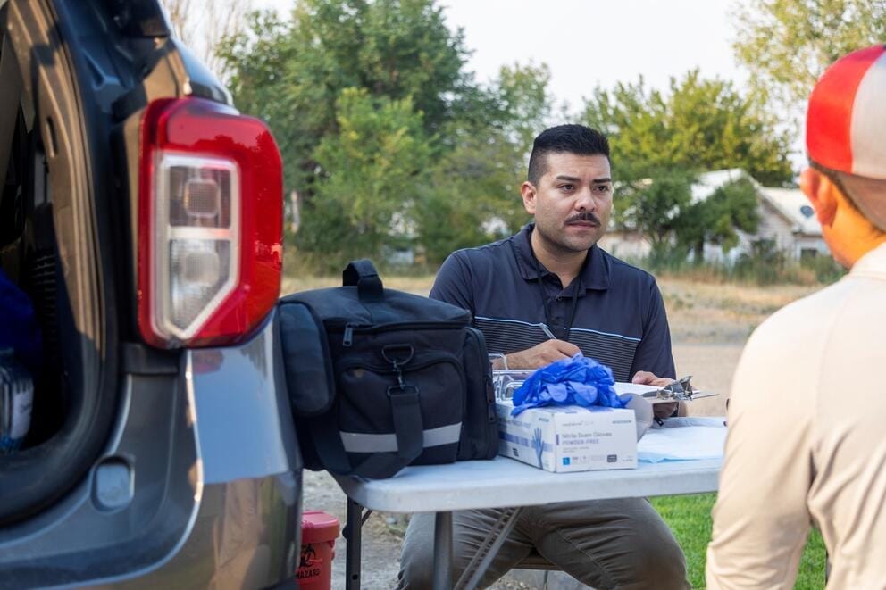 A person sits at a table with medical equipment in an outdoor field