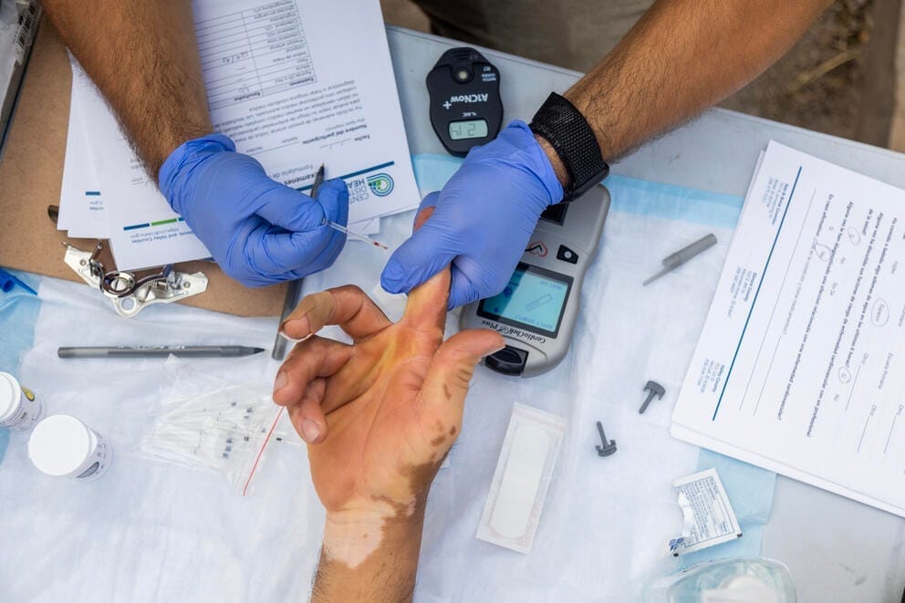 A person with gloves gets a blood sample from another person's finger.