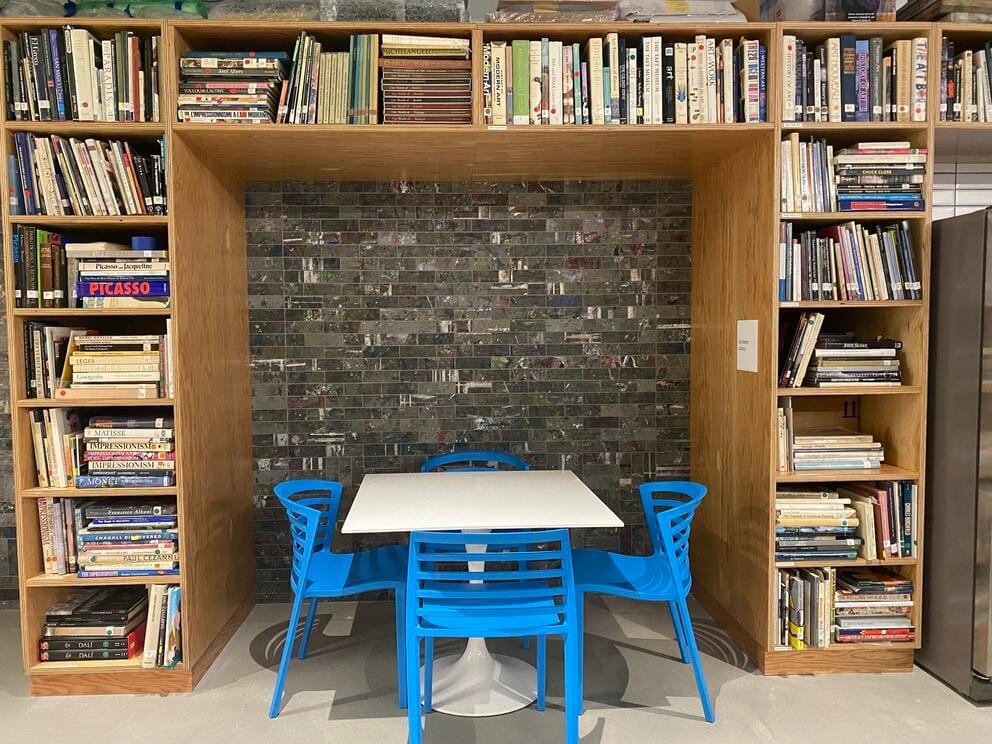 photo of a white table and blue chairs surrounded by bookcases filled with art books