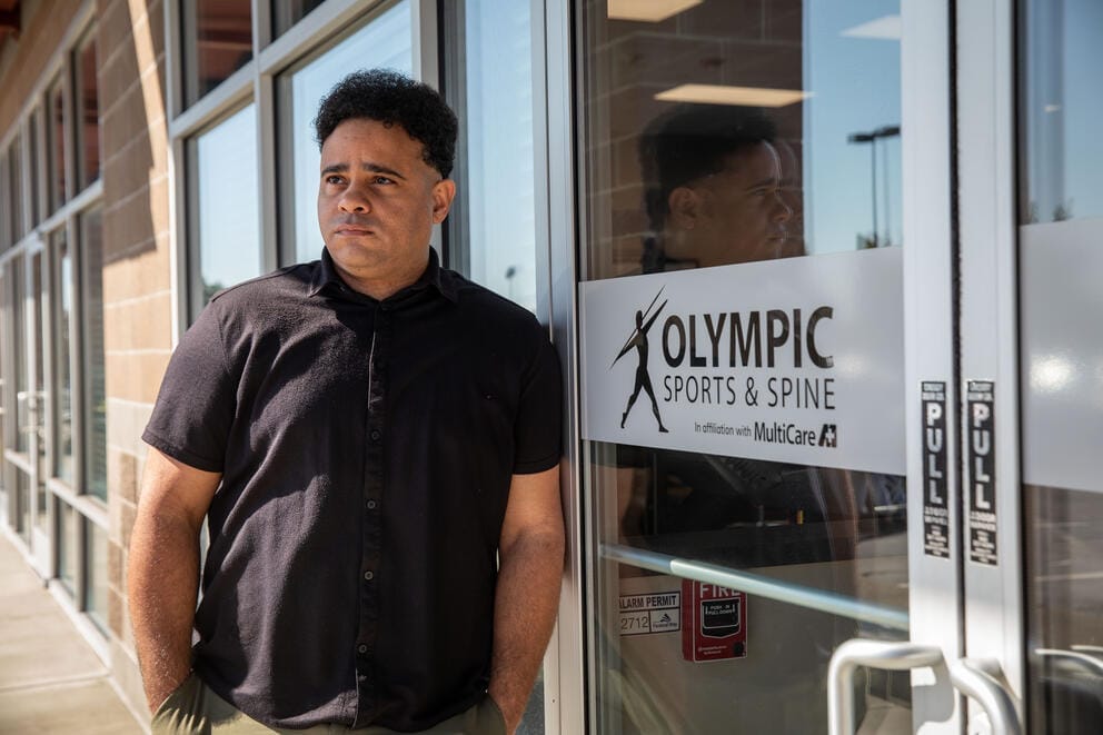 Juan Bloise poses outside the glass door to a physical rehabilitation center.