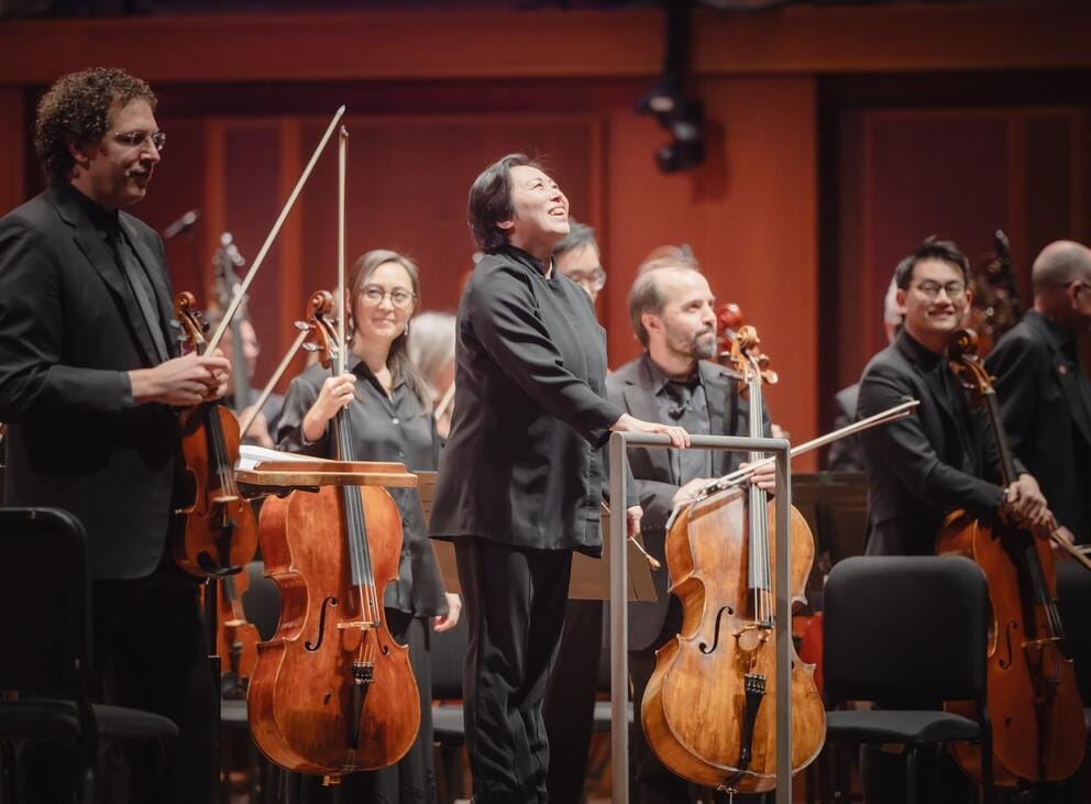 a woman conductor on stage wearing black, surrounded by symphony musicians