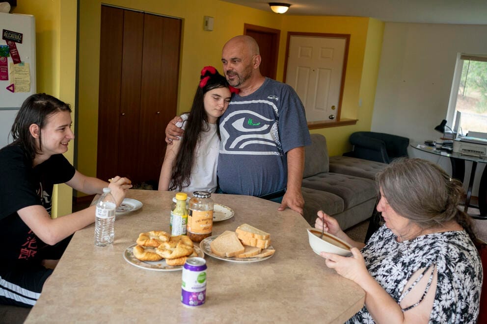 A father hugs his daughter at a table where his son and wife are eating soup