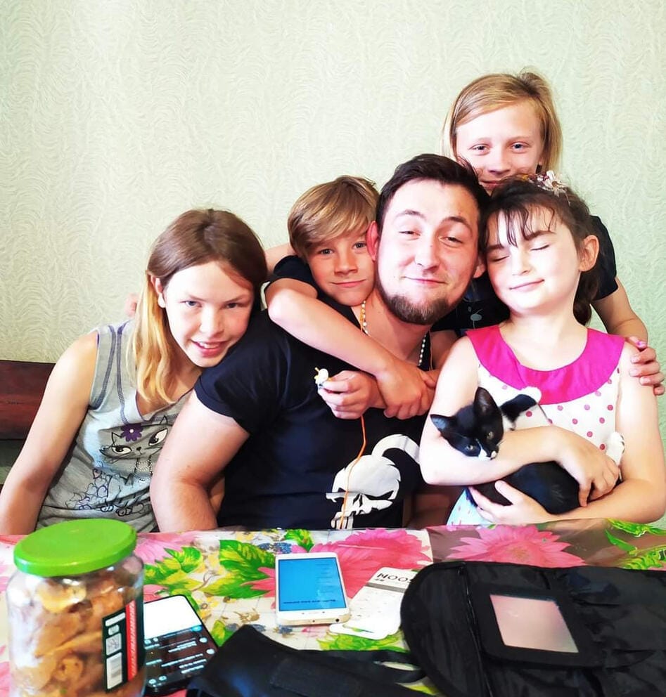 A group photo of a young man sitting with four children around him, hugging him.