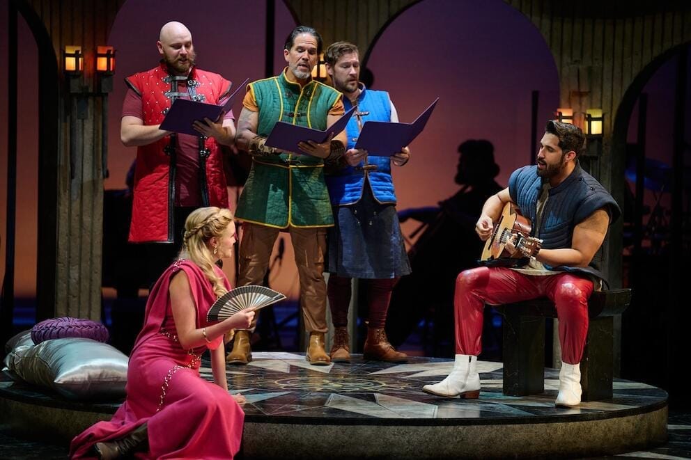 people on stage in theatrical costumes, including a woman in a medieval gown