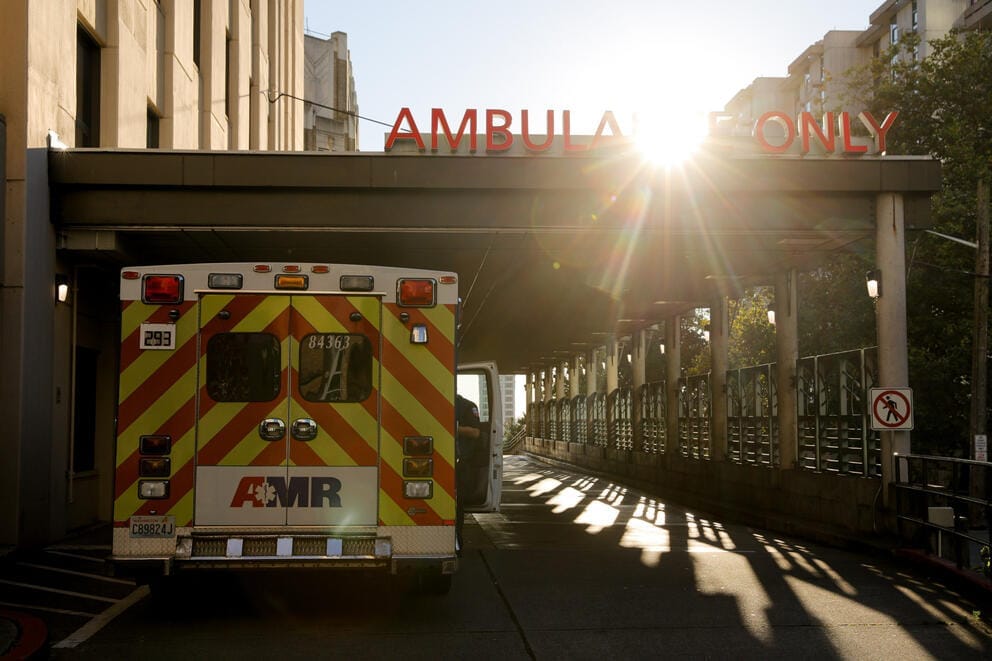 A sunburst shines over an ambulance outside an emergency room