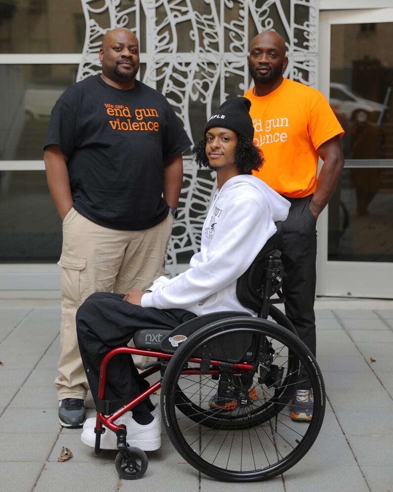 A portrait of three Black men, the youngest one at center is in a wheelchair