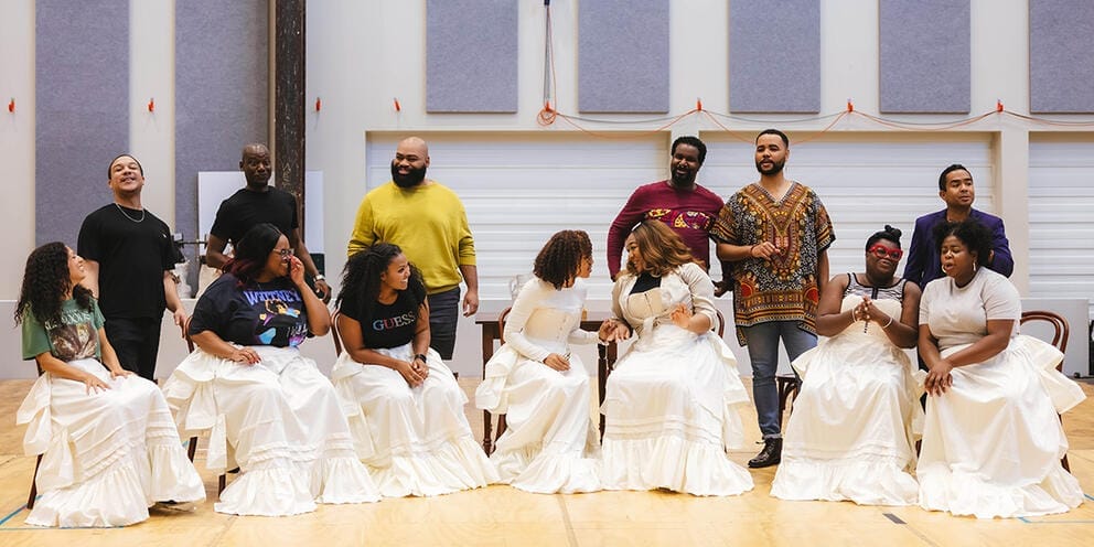 photo of a group of performers rehearsing on stage, the women wearing white skirts