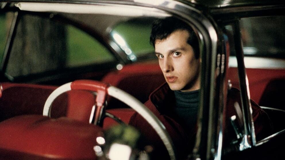 still from the horror movie Christine featuring a young man sitting in a vintage car