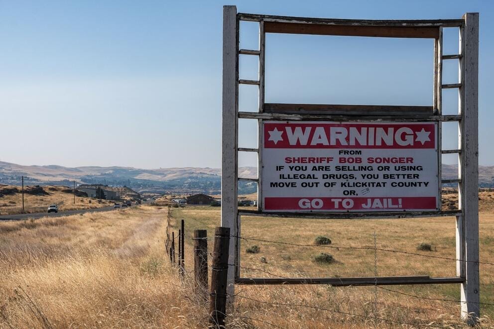 A sign that warns drug dealers and users that they will go to jail stands in a field.