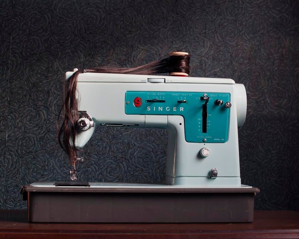 an old Singer sewing machine with a lock of brown hair threaded through it