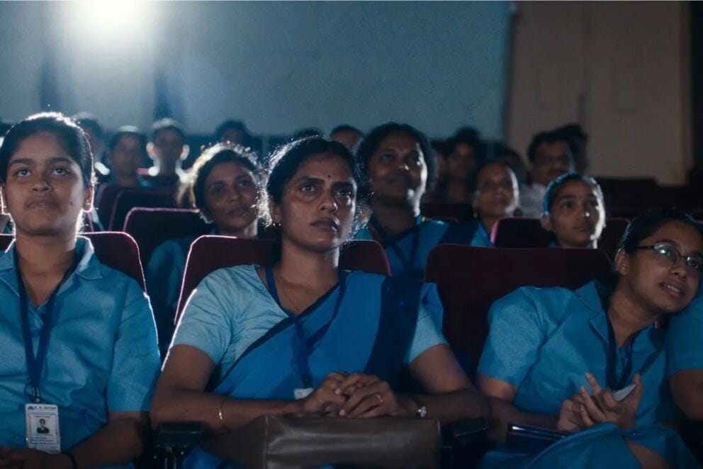 film still showing women wearing blue saris sitting in a movie theater watching a film