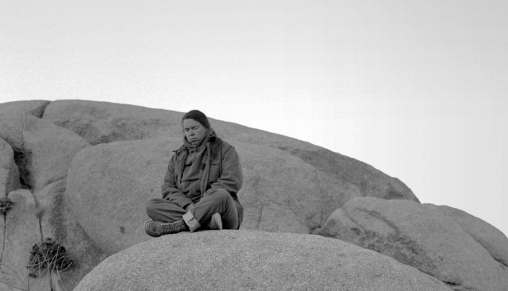 black and white photo of a woman sitting with eyes closed on smooth rocks