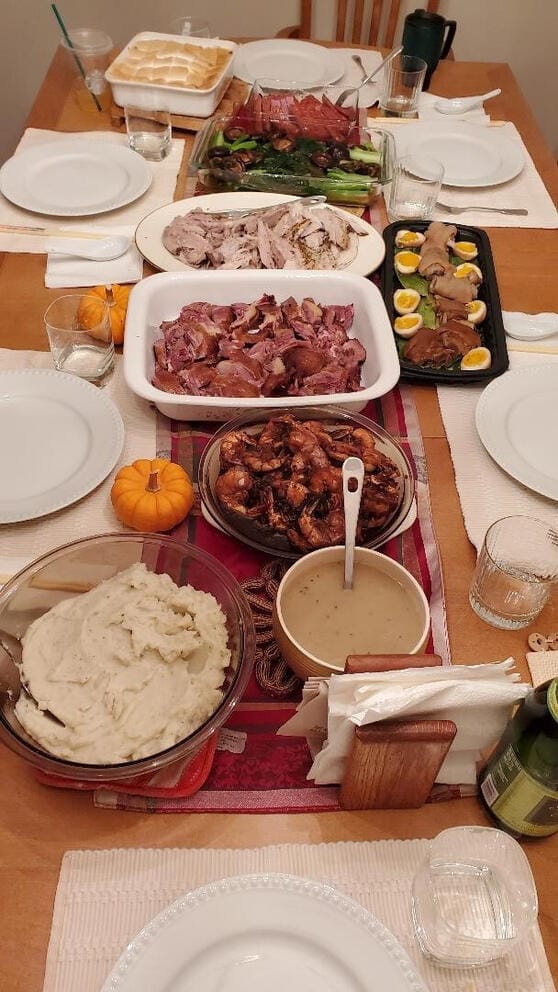 Chloe Fong, a Chinese-American in Seattle, had a 2023 Thanksgiving meal with family including both Cantonese and American dishes. Between the sliced ham and turkey is a dish of mushrooms and gailan, or Chinese broccoli, (second from top) and braised pigs’ feet with soft-boiled eggs (right, in black rectangle dish). Next to the mashed potatoes and gravy are dishes of stir-fried shrimp and pieces of roast duck (center). There was also marshmallow-covered mashed yams (top left) and rice (not shown). “We always